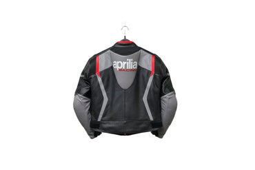 Detailed view of the Aprilia Racing chest logo, Akrapovič patch, and slate grey leather panels on a professional racing jacket.