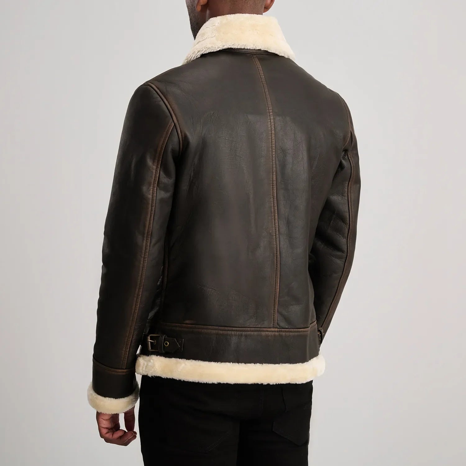 Back of a brown leather shearling jacket, detailing the vertical seam lines and the soft white wool trim along the bottom edge.