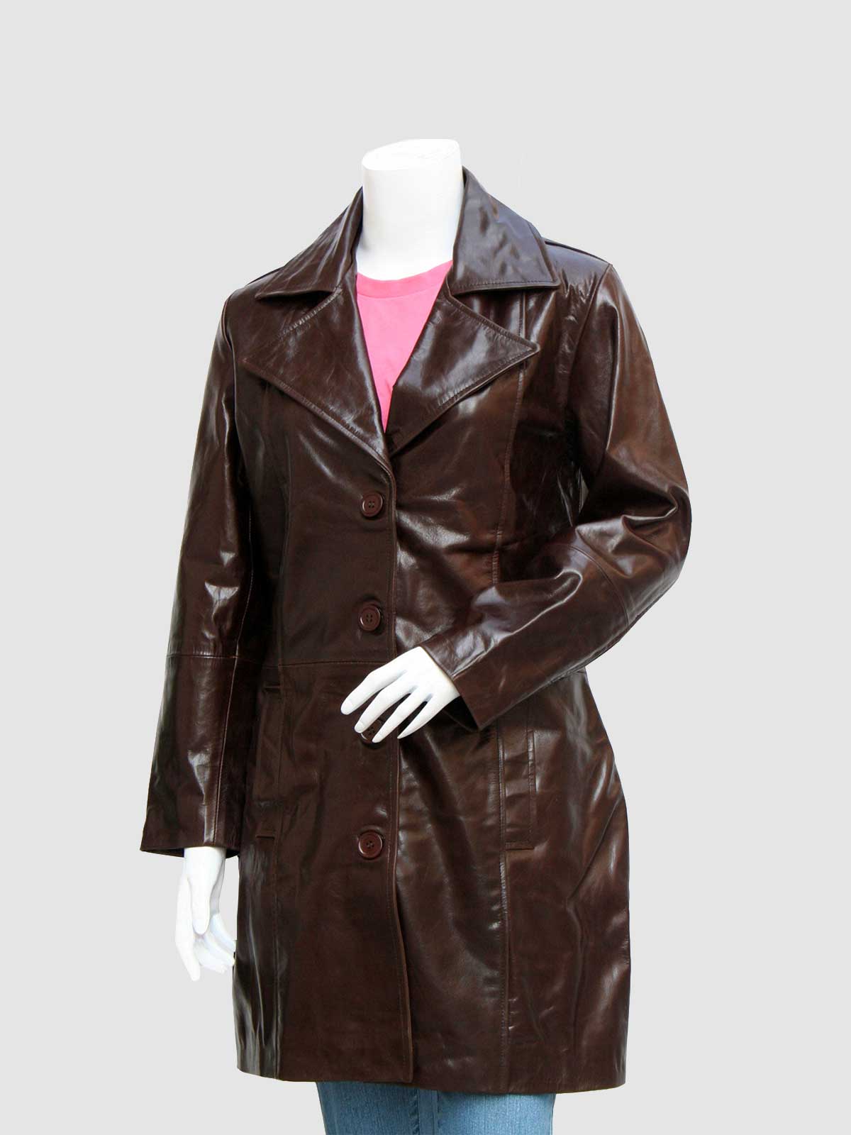 Front profile of a long, shiny brown leather coat for women, secured by three large buttons, worn over a pink shirt and blue jeans.