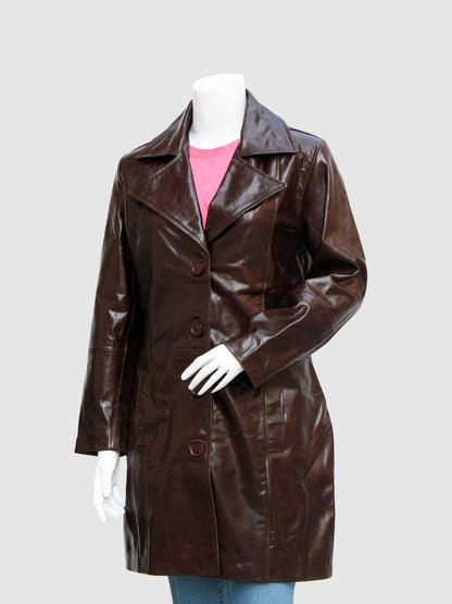Front profile of a long, shiny brown leather coat for women, secured by three large buttons, worn over a pink shirt and blue jeans.