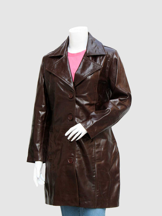 Front profile of a long, shiny brown leather coat for women, secured by three large buttons, worn over a pink shirt and blue jeans.