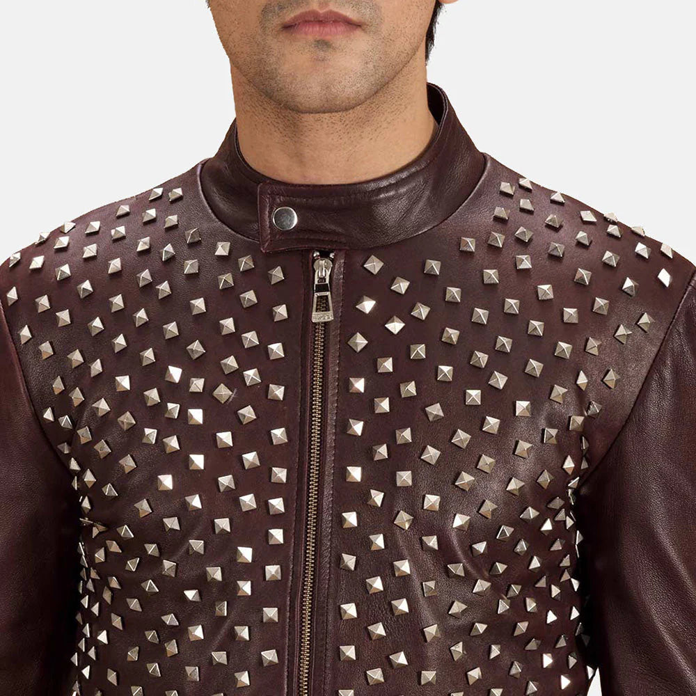 Front view of a man modeling a dark maroon leather jacket, completely covered in dense, all-over silver pyramid stud embellishments.