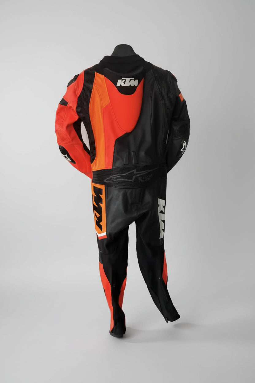 Detailed view of the KTM Racing chest logo, perforated leather panels, and accordion stretch sections on a professional racing suit.