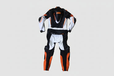 Detailed view of the KTM Ready to Race chest logo, Akrapovič patch, and orange accordion stretch panels on a professional racing suit.