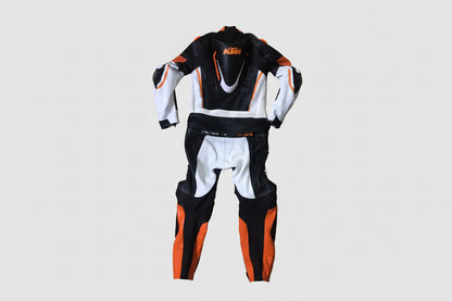 Detailed view of the KTM Ready to Race chest logo, Akrapovič patch, and orange accordion stretch panels on a professional racing suit.